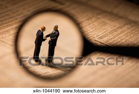 Miniature businessmen, seen through magnifying glass, shake hands while sstanding on financial newspaper View Large Photo Image Stock Image - Miniature businessmen, seen through magnifying glass, shake hands while sstanding on financial newspaper. Fotosearch