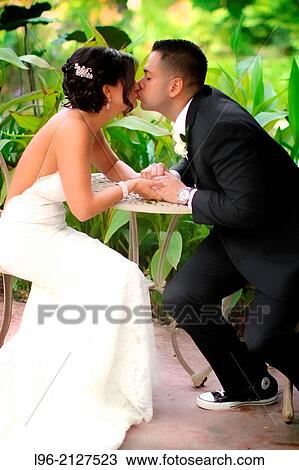 Stock Image - mixed race couple holding hands and kissing while sitting in a garden. Fotosearch