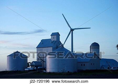 Modern grain handling facility with wind generator towering over it on Iowa farmstead near Williams, Iowa, USA Photo shows grain elevator tall structure, round metal grain bins, gas grain dryer, silo and wind generator at twilight View Large Photo Image Stock Photograph - Modern grain handling facility with wind generator towering over it on Iowa farmstead near Williams, Iowa, USA Photo shows grain elevator tall structure, round metal grain bins, gas grain dryer, silo and wind generator at twilight. Fotosearch