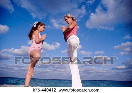 Stock Image - Mom and daughter practice yoga at beach. Fotosearch