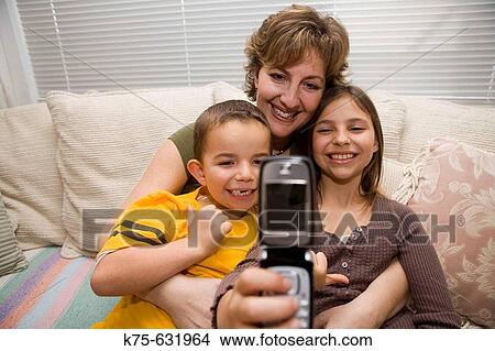 Mom holding two children and taking photo with camera phone View Large Photo Image Picture - Mom holding two children and taking photo with camera phone. Fotosearch