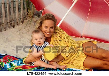 Mom with her toddler son under beach umbrella View Large Photo Image Picture - Mom with her toddler son under beach umbrella. Fotosearch