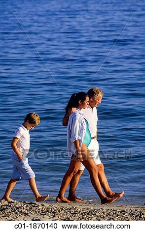 Stock Image - Moody boy walking behind couple with pregnant woman on beach. Fotosearch