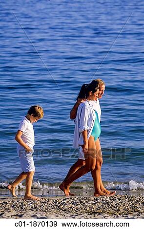 Moody boy walking behind couple with pregnant woman on beach View Large Photo Image Stock Photo - Moody boy walking behind couple with pregnant woman on beach. Fotosearch
