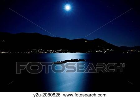 Stock Photograph - Moon light reflected over an alpine lake maggiore with brissago islands and mountains at night in ticino switzerland.. Fotosearch