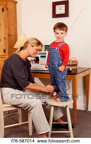 Mother altering clothes by sewing up cuff of son's overalls. View Large Photo Image Picture - Mother altering clothes by sewing up cuff of son's overalls.. Fotosearch