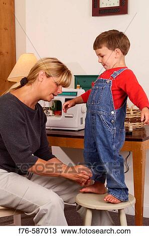 Stock Image - Mother altering clothes by sewing up cuff of son's overalls.. Fotosearch