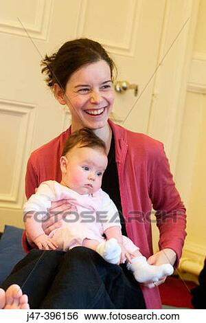 Stock Photograph - Mother and baby sitting on the floor laughing. Fotosearch