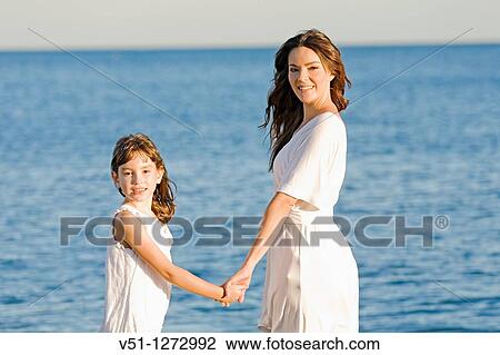 Mother and daughter holding hands and looking at camera at the beach View Large Photo Image Stock Image - Mother and daughter holding hands and looking at camera at the beach. Fotosearch