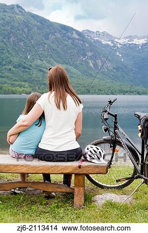 Mother and daughter together sitting on a wooden bench by the lake of Bohinj, Slovenia Gorenjska. View Large Photo Image Picture - Mother and daughter together sitting on a wooden bench by the lake of Bohinj, Slovenia Gorenjska.. Fotosearch