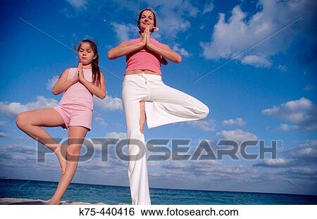 Stock Photograph - Mother and daughter yoga at beach. Fotosearch