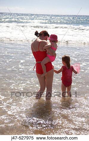 Stock Photography - Mother and daughters, aged 2 and 4, standing paddling in the sea. Fotosearch
