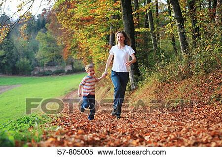 Stock Photography - Mother and son running hand in hand on path full of leaves in fall, having fun and laughing, autumn foliage covering path in forest, autumn, fall, Zuerich, Switzerland. Fotosearch