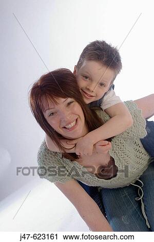 Stock Image - Mother and son, three quarter shot, 3 year old boy on his mums shoulders, smiling into camera.. Fotosearch