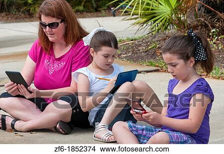 Picture - Mother and two daughters aged 6 and 8 playing and learning in front of home relaxing with games and computers learning. Fotosearch