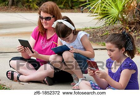 Stock Image - Mother and two daughters aged 6 and 8 playing and learning in front of home relaxing with games and computers learning. Fotosearch