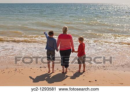 Stock Image - Mother and two sons stand on a UK beach looking out to sea in the summer. Fotosearch