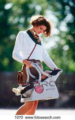 Stock Image - Mother carrying baby in car seat. Fotosearch