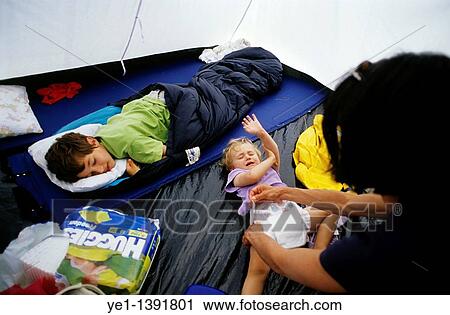 Stock Image - Mother changing the nappy of a crying baby girl inside a tent next to her sleeping brother. Fotosearch