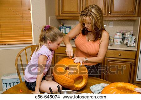 Picture - Mother helps daughter carve a halloween pumpkin.. Fotosearch