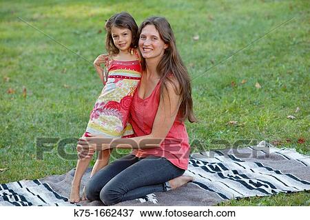 Mother hugging young daughter on blanket on lawn View Large Photo Image Stock Photo - Mother hugging young daughter on blanket on lawn. Fotosearch