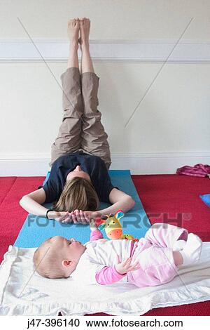 Stock Image - Mother in post natal yoga class with her baby. Fotosearch