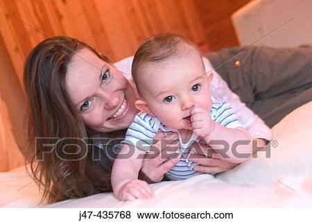 Mother lying down with 5 month old baby boy smiling into camera, boy, sucking his thumb View Large Photo Image Stock Photo - Mother lying down with 5 month old baby boy smiling into camera, boy, sucking his thumb. Fotosearch