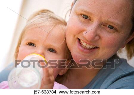 Mother sitting with daughter while drinking a bottle. View Large Photo Image Picture - Mother sitting with daughter while drinking a bottle.. Fotosearch