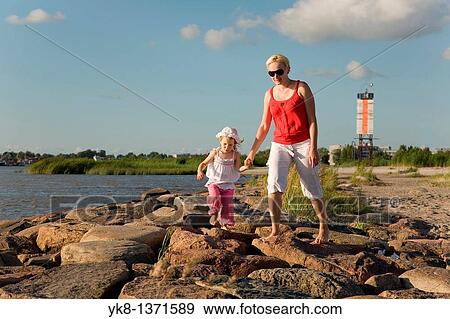 Stock Photo - Mother with Kid Girl Holding Hands Walking on P? rnu Pier by Sea, Estonia. Fotosearch