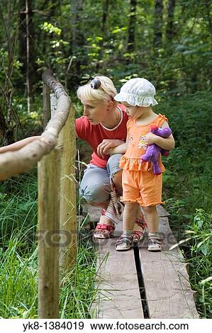 Stock Photo - Mother with Kid Girl Standing on Wooden Boardwalk with Fence in Forest. Fotosearch