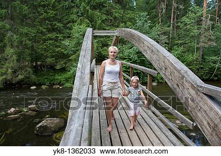 Stock Image - Mother With Kid Walking Over Wooden Bridge Holding Hands, P? lva County, Estonia, Europe. Fotosearch