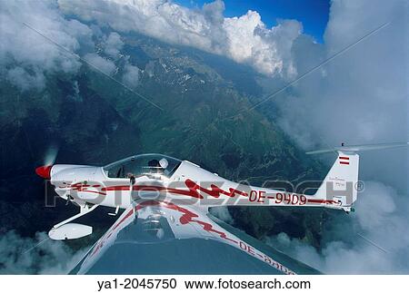 Stock Image - Motorglider plane Super Dimona flying near clouds over Pyrenees mountains, north of Jaca, Aragon, Spain.. Fotosearch
