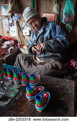 Stock Photo - Mr. Tendup, aged 88 years in 2010 CE, makes woolen baby shoes at the Tibetan refugee self help centre in Darjeeling, West Bengal, India.. Fotosearch