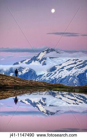 Stock Image - Mt Aspiring, tramper enjoys moonrise at dusk, Cascade Saddle tarn, Mount Aspiring National Park, Otago, New Zealand. Fotosearch