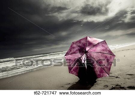 Stock Photo - Mujer con paraguas sentada en la playa tras la tormenta.. Fotosearch