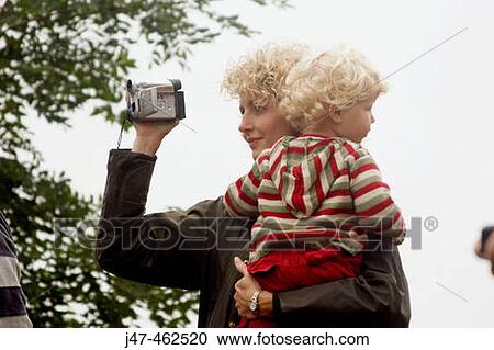 Mum filming at a sports day, holding a child in her arms View Large Photo Image Stock Image - Mum filming at a sports day, holding a child in her arms. Fotosearch