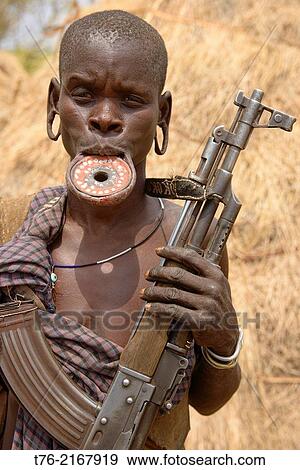 Mursi woman with lip plate and Kalashnikov in the Lower Omo Valley of Ethiopia. The Mursi girls have a fold cut in their lower lip as they enter womanhood, where a pulley is inserted, which then stretches the lip until larger plates can be put in. View Large Photo Image Stock Photo - Mursi woman with lip plate and Kalashnikov in the Lower Omo Valley of Ethiopia. The Mursi girls have a fold cut in their lower lip as they enter womanhood, where a pulley is inserted, which then stretches the lip until larger plates can be put in.. Fotosearch