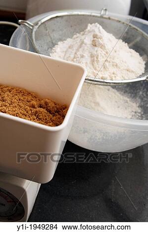 Muscovado sugar on weighing scales with flour in sieve. View Large Photo Image Picture - Muscovado sugar on weighing scales with flour in sieve.. Fotosearch