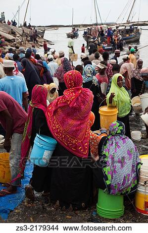 Picture - Muslim women with colorful headscarfs waiting for the fishermen turning back from the catch at the daily fish market, Stone Town, Unguja Island, Zanzibar Archipelago, Tanzania, East Africa.. Fotosearch
