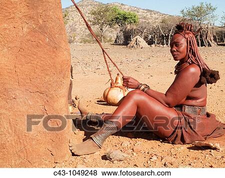 Namibia - Himba woman with the typical leather headdress of the married women agitates a pot of cow milk in order to turn the milk into butter fat In a village near the Epupa Falls Kaokoland, Kunene region, northern Namibia View Large Photo Image Stock Photo - Namibia - Himba woman with the typical leather headdress of the married women agitates a pot of cow milk in order to turn the milk into butter fat In a village near the Epupa Falls Kaokoland, Kunene region, northern Namibia. Fotosearch