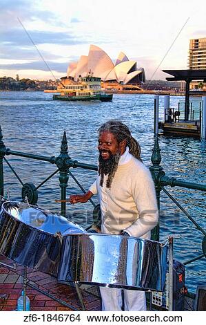 Picture - Native black man playing steel drum at harbor of Sydney Opera House Australia. Fotosearch