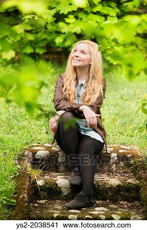 Nature scene with one young attractive blonde woman sitting in a park looking up. View Large Photo Image Stock Image - Nature scene with one young attractive blonde woman sitting in a park looking up.. Fotosearch