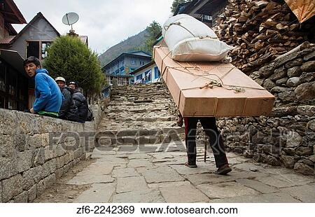 Stock Photo - Nepal Himalayas Porter carrying massive load through the streets of Phak Ding Solukhumbu remote Mt Everest 55 56.. Fotosearch
