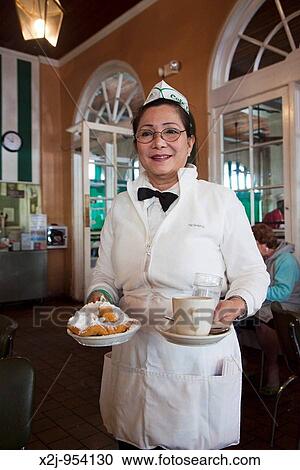 Stock Image - New Orleans, Louisiana - A waitress at Cafe du Monde serves cafe au lait and beignets, a fried pastry with a generous covering of powdered sugar. Fotosearch
