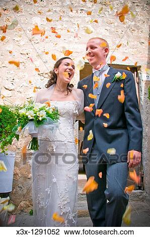 Stock Image - Newlywed couple with thrown flower petals after service. Fotosearch