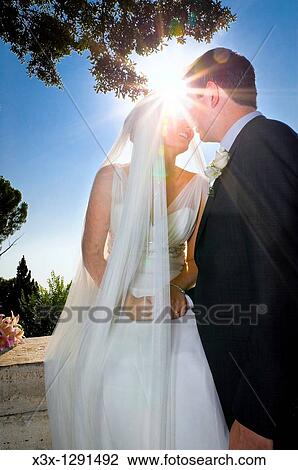 Stock Image - Newlyweds kissing against the sun. Fotosearch