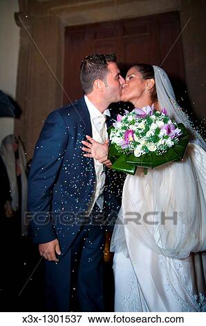 Newlyweds kissing during rice throwing after wedding ceremony View Large Photo Image Stock Photo - Newlyweds kissing during rice throwing after wedding ceremony. Fotosearch