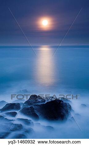 Stock Image - Night view of the moon rising over the sea. Fotosearch