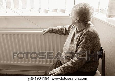 Picture - Ninety year old lady with hand on radiator looking out of window England, United Kingdom. Fotosearch