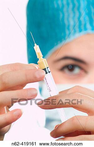 Nurse with the white mask and blue hat check that there is no air inside the syringe with the medicine View Large Photo Image Stock Image - Nurse with the white mask and blue hat check that there is no air inside the syringe with the medicine. Fotosearch